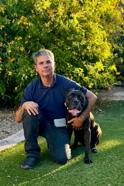Win kneeling next to a black dog on a sunny lawn